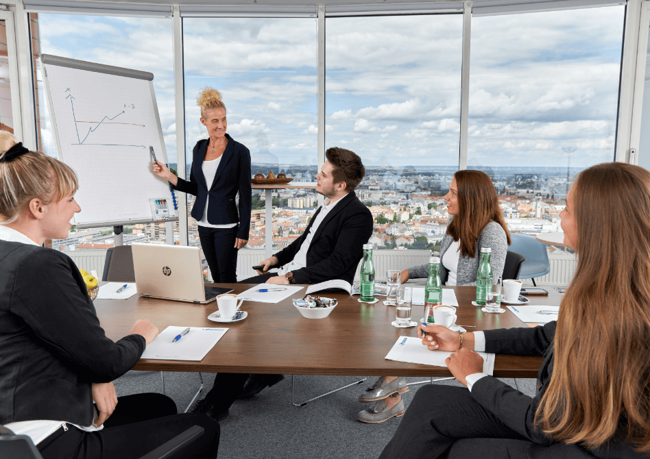A diverse business team collaborating and listening to a presentation during a meeting in a high-rise office with a city view.