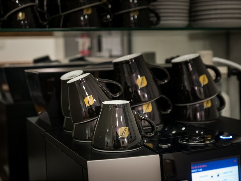 Gestapelte schwarze Kaffeetassen mit Logo auf einer modernen Kaffeemaschine im Café
