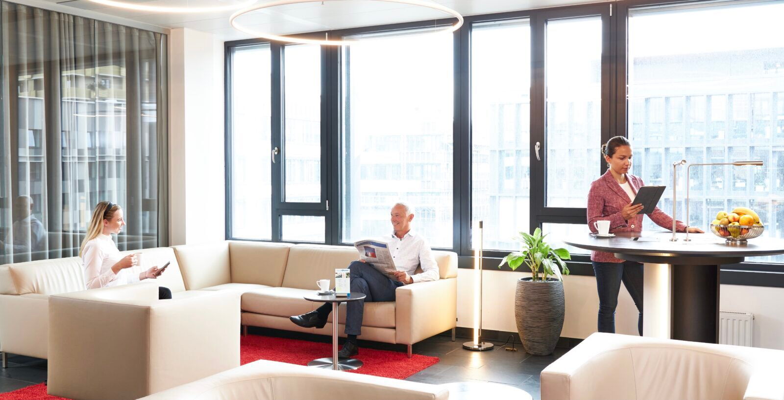 Mitarbeiter arbeiten und entspannen in einem hellen, modernen Büro-Loungebereich mit großen Fenstern