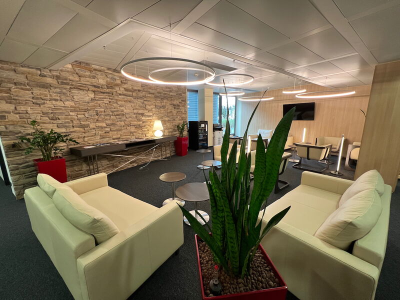 Geräumiger Loungebereich im Büro mit cremefarbenen Sofas, runden Leuchten, einer rustikalen Steinwand und Grünpflanzen.