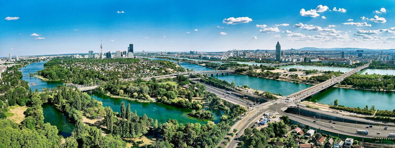 Panoramablick auf die Wiener Skyline mit der Donau, Brücken und grünen Parks unter blauem Himmel