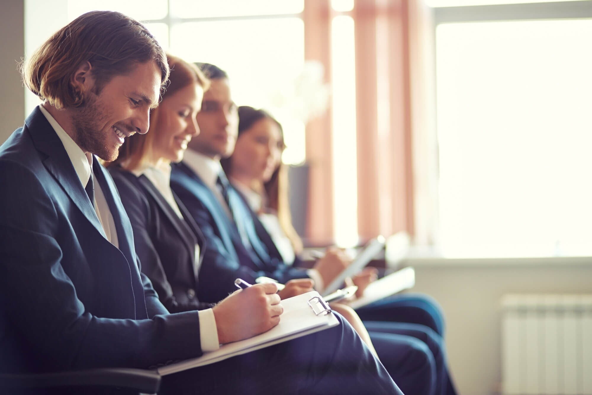 A line of smiling co-workers taking notes on clipboards during a corporate seminar or meeting