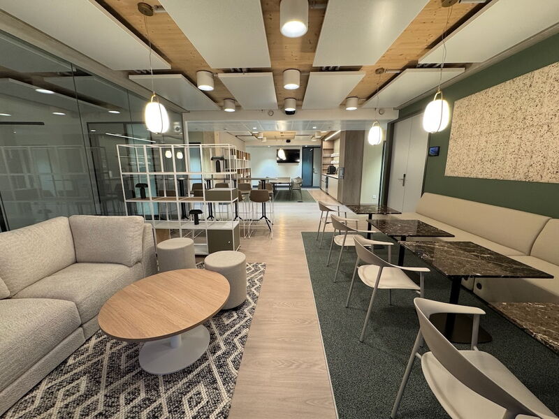 Spacious modern office breakout area featuring comfortable seating, couches, coffee tables, and stylish lighting.