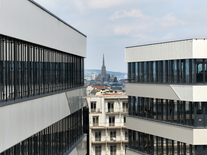 Blick durch zwei moderne weiße Bürogebäude im QBC Wien auf die historische Skyline mit dem Stephansdom