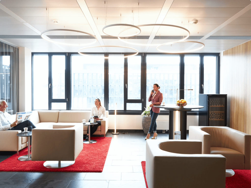 Employees relaxing and working in a modern, well-lit office lounge with contemporary furniture and large windows