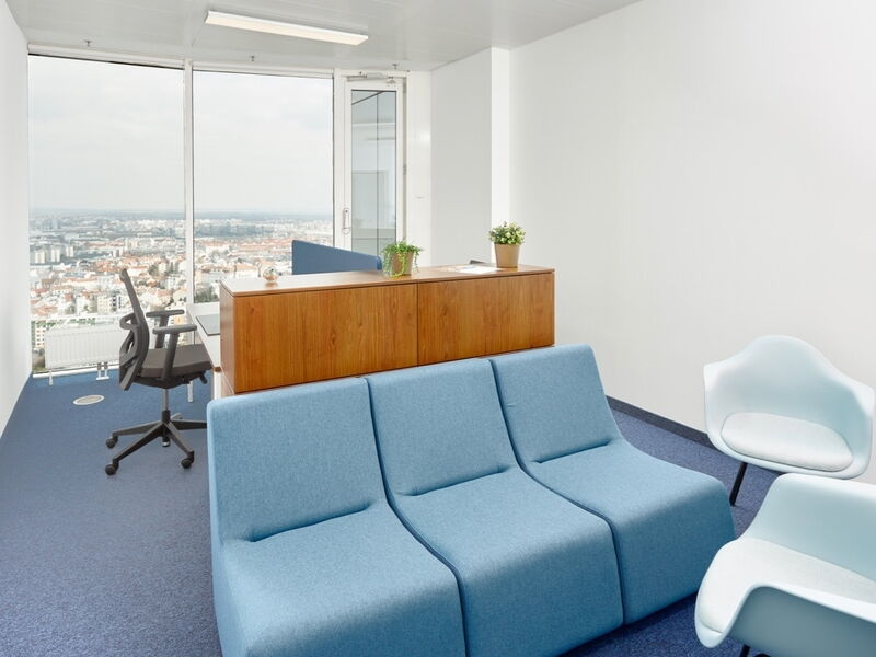 Helles, modernes Büro mit blauem Modulsofa, Holzkommode, Bürostuhl und Panoramablick auf die Stadt durch große Fenster.