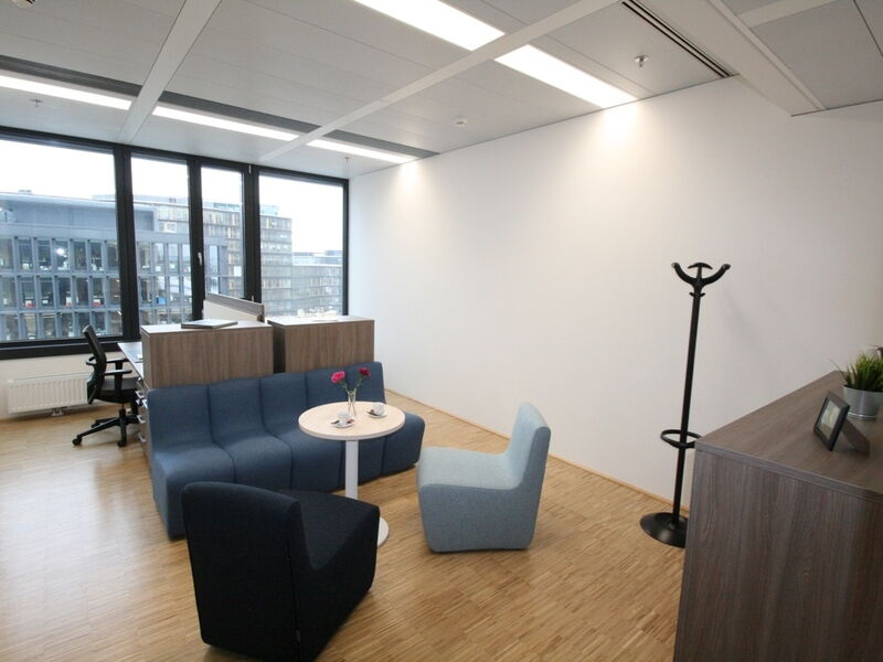 Heller und moderner Loungebereich im Büro mit blauen Sitzmöbeln, einem runden Tisch und Holzakzenten.