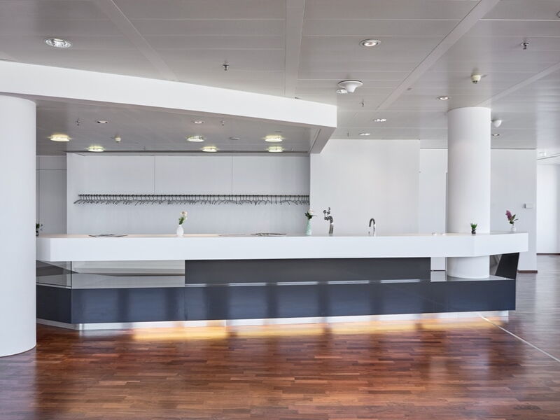Elegante und moderne Unternehmensrezeption mit schwarz-weissem Design, Holzboden und grossen Fenstern mit Weitblick in einem hellen Buerobereich.