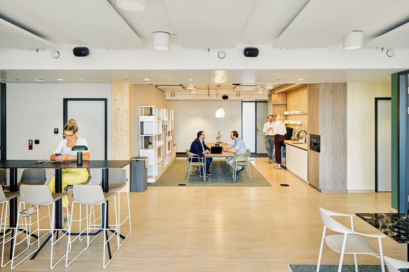 Employees working and collaborating in a modern, brightly lit open-plan office space featuring a kitchenette and meeting area.