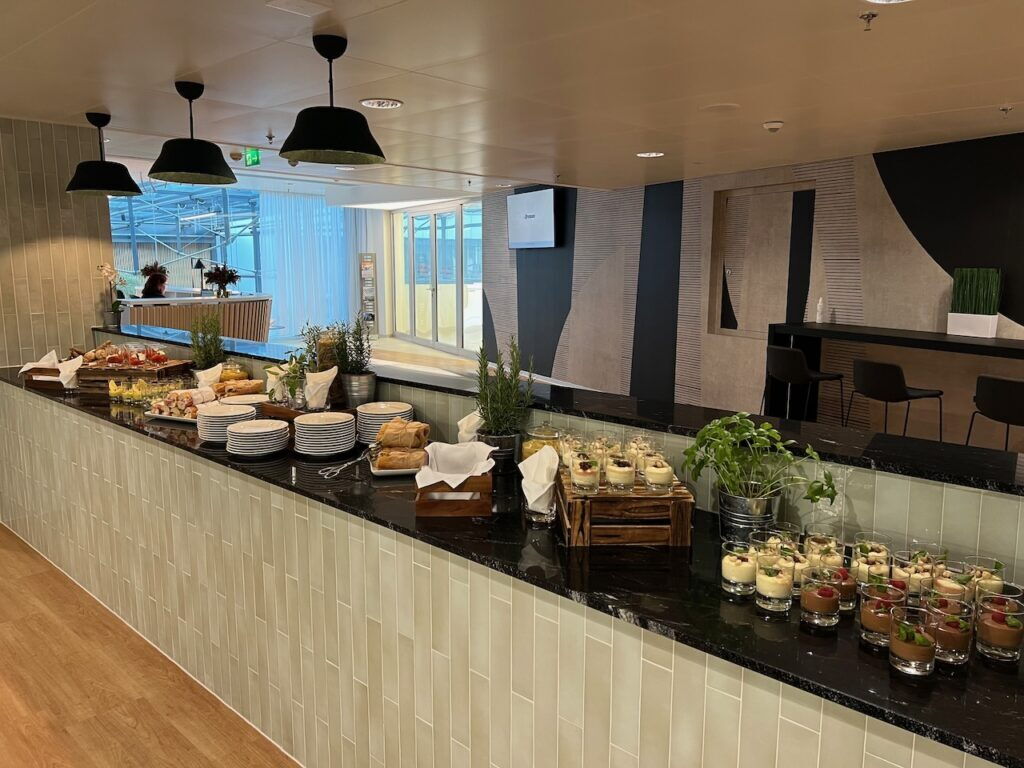 A long black buffet counter in a modern office canteen filled with plates, fresh herbs, and small dessert glasses.