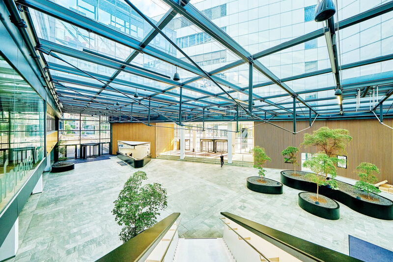 Geräumiges, modernes Bürogebäude-Atrium mit großer Glaskonstruktion, Holzverkleidung, Innenbäumen und Empfangsbereich im EuroPlaza
