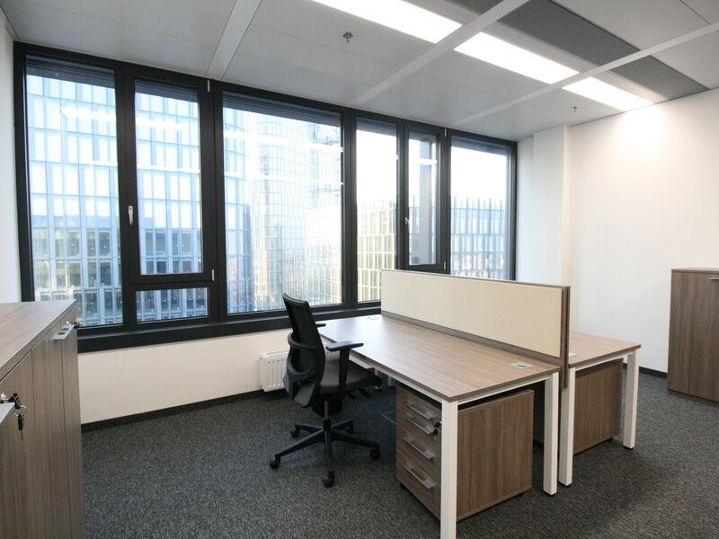 Heller, moderner Büroraum ausgestattet mit Holztischen, ergonomischem Bürostuhl und großen Fenstern mit Blick auf Wolkenkratzer.