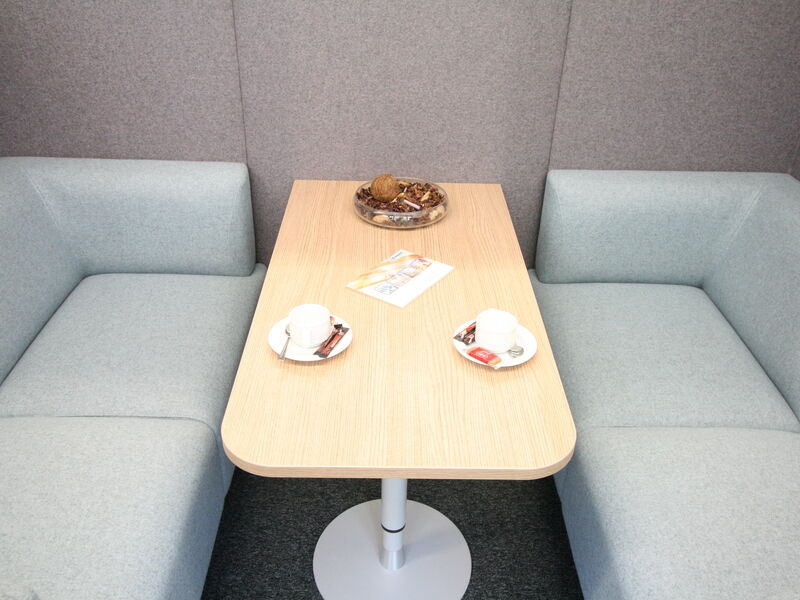 Moderne Büro-Besprechungsnische mit hellblauen Polstersofas, einem Holztisch mit Kaffeetassen und Akustik-Wandpaneelen