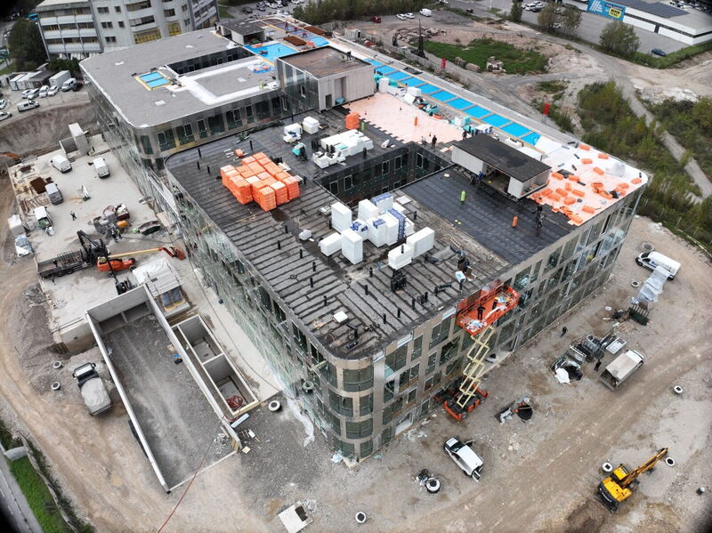 Luftaufnahme per Drohne von der Baustelle des YOUR OFFICE Campus Noricum mit sichtbaren Dämmarbeiten auf dem Dach und Glasfassaden.