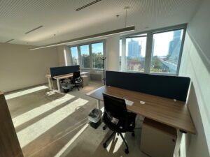 Bright modern office interior with wooden desks, ergonomic chairs, and large windows overlooking the city