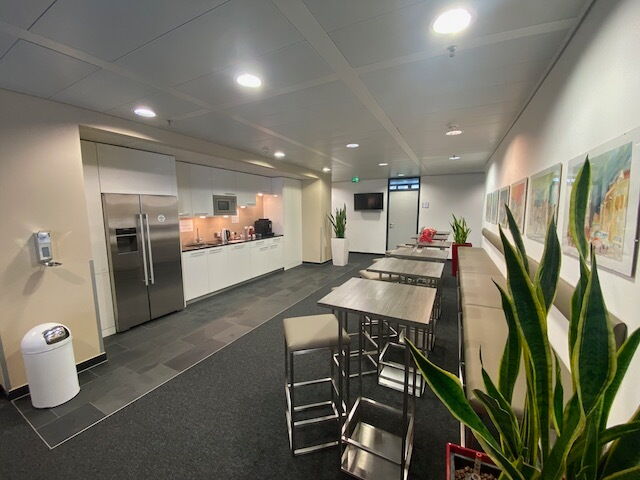 Spacious and modern office kitchen and breakroom featuring high tables, a stainless steel refrigerator, and kitchenette facilities.
