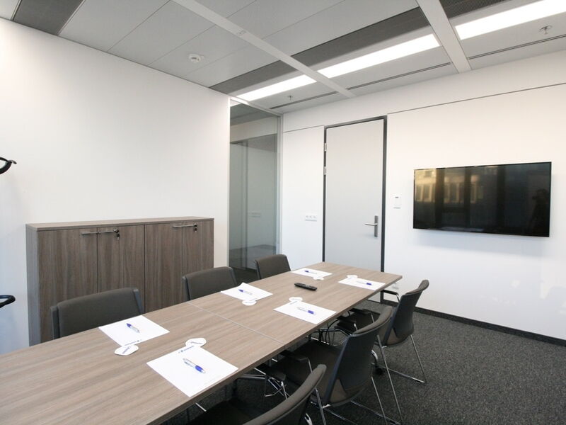 Geräumiger und moderner Konferenzraum mit Tischen, Stühlen, Flipcharts und flexiblen Trennwänden in einem Bürogebäude.