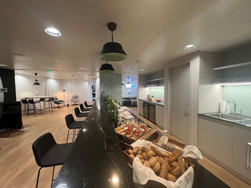 Eine moderne Büro-Teeküche mit einer schwarzen Marmortheke voller frischem Brot und Snacks, umgeben von Sitzgelegenheiten und dezenter Beleuchtung.