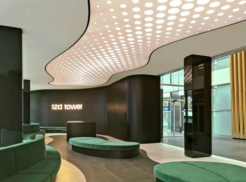 Modern interior of the IZD Tower lobby featuring a curved illuminated ceiling with dot patterns, dark ribbed walls, and green lounge seating.