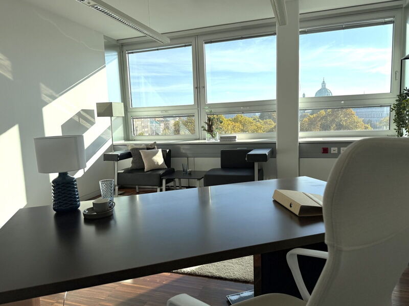 Helles Executive Büro im YOUR OFFICE Akademiehof mit einem modernen Schreibtisch, einer Sitzecke und großen Fenstern mit Panoramablick auf die Stadt.