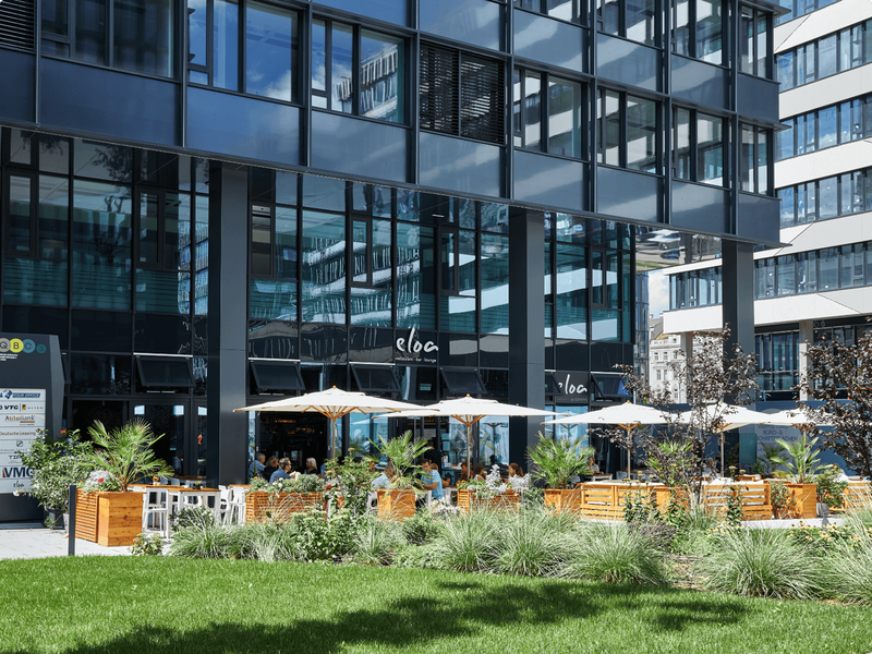 Außenterrasse mit Sonnenschirmen und Pflanzen vor dem modernen Restaurant Eloa am QBC in Wien