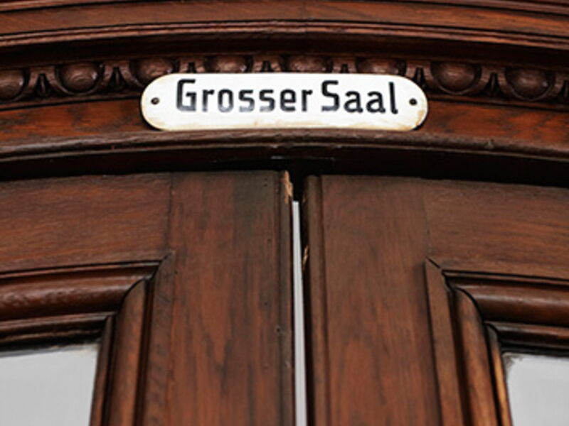 Nahaufnahme einer historischen Holztür mit einem Schild mit der Aufschrift Grosser Saal darüber