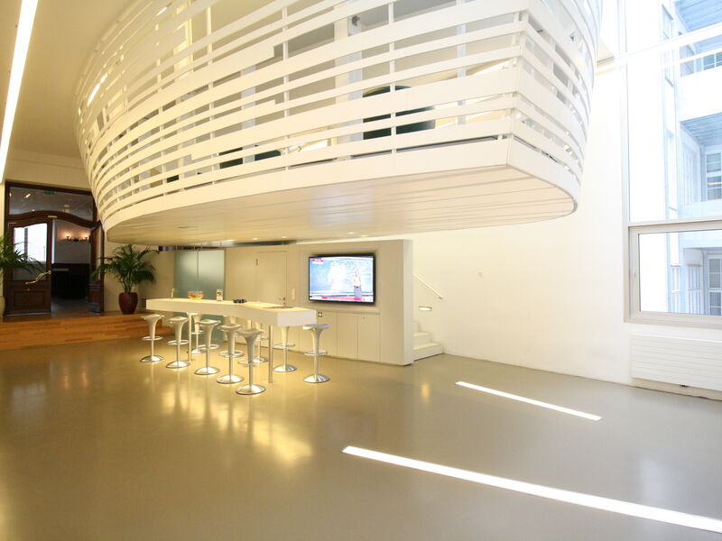Geräumiges, modernes Büro mit einer großen, weißen schwebenden Struktur, einer Bartheke mit Hockern und großen Fenstern.