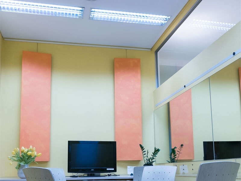 Moderne Büro-Besprechung mit gelben Wänden, vertikalen orangen Akustikpaneelen, einem Tischmonitor und Stühlen.