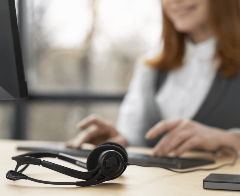 Lächelnde Callcenter-Mitarbeiterin tippt auf Tastatur mit schwarzem Headset im Vordergrund