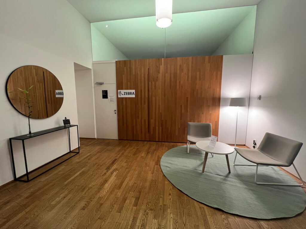 Modern office lobby featuring wooden wall paneling, a round mirror, a green rug, and comfortable seating with a coffee table.
