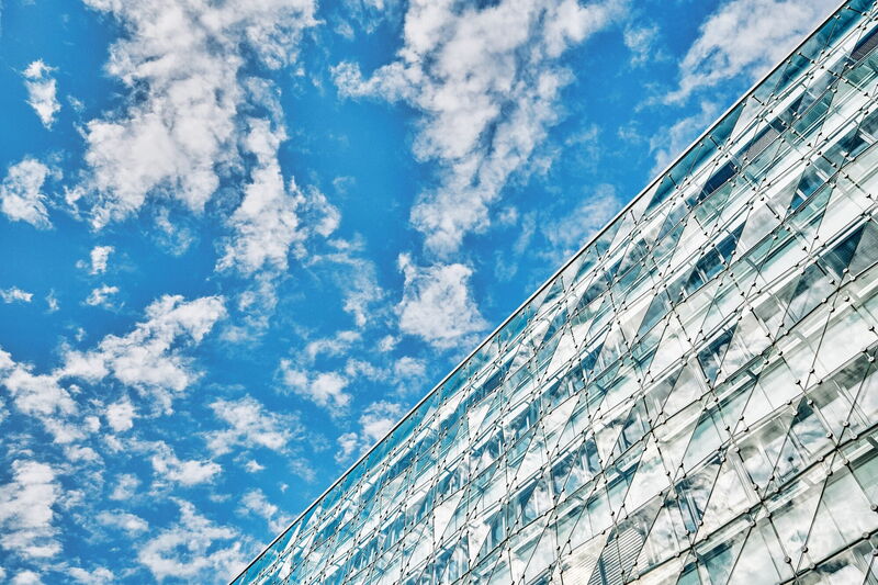 Froschperspektive auf die moderne Glasfassade des EuroPlaza mit spiegelnden Wolken und blauem Himmel
