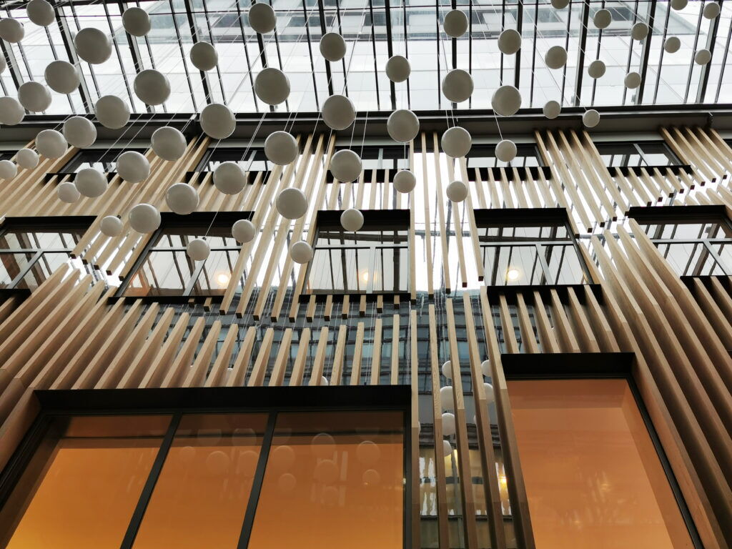 Modernes Innendesign des IZD Towers mit hängenden weißen Kugeln und vertikalen Holzlamellen im Atrium
