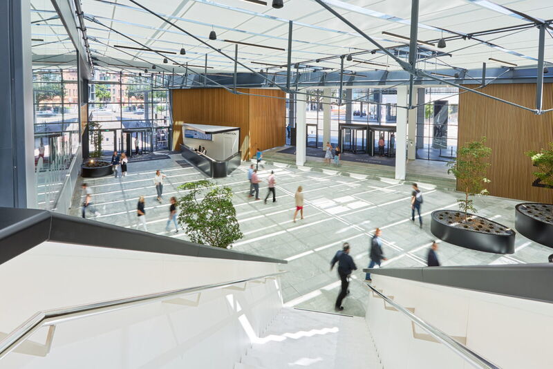 Helle und moderne Büro-Eingangshalle mit Glasdecke, Holzverkleidung und Menschen, die durch das Foyer gehen.