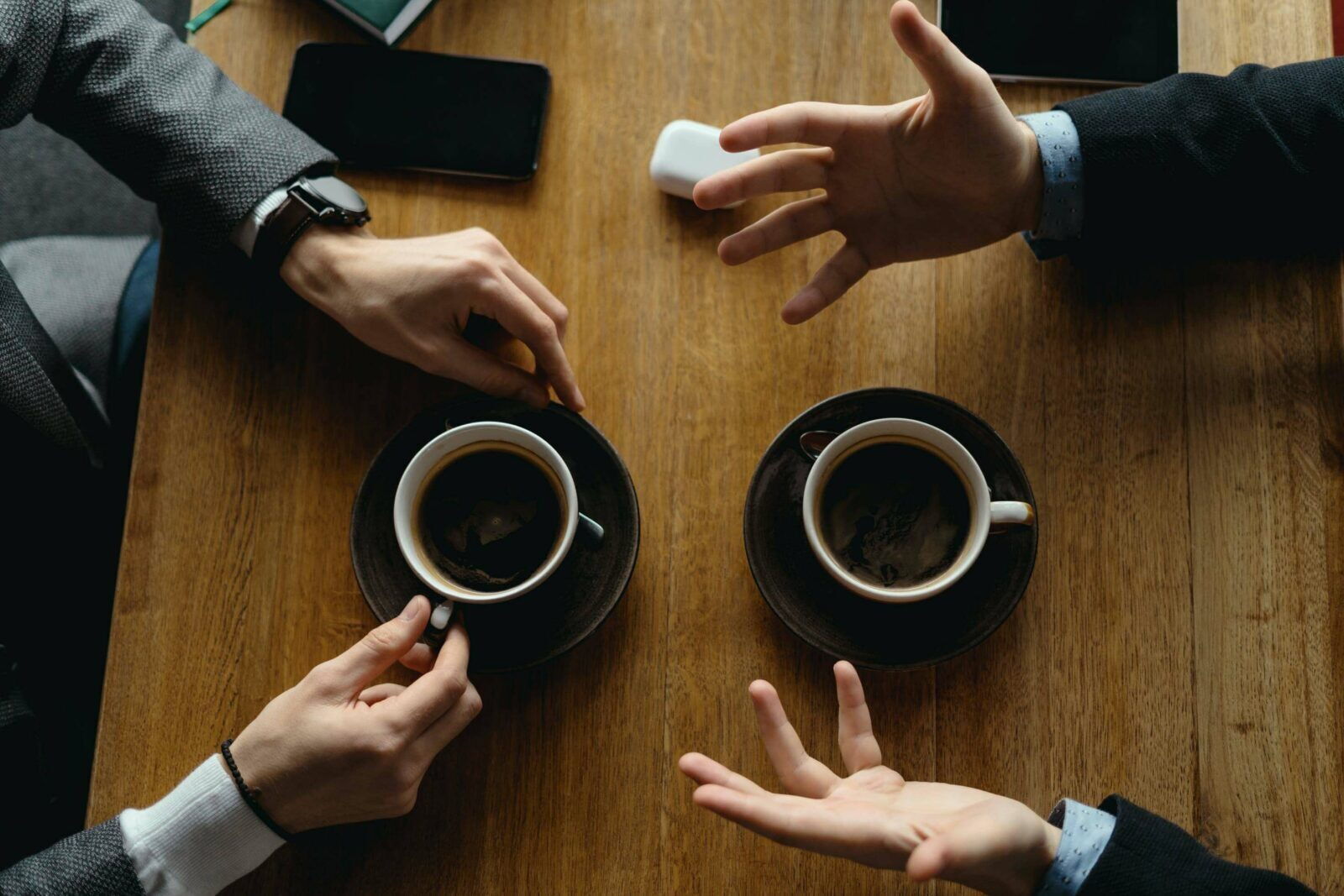 Two people having a professional interview meeting across a wooden table with coffee cups