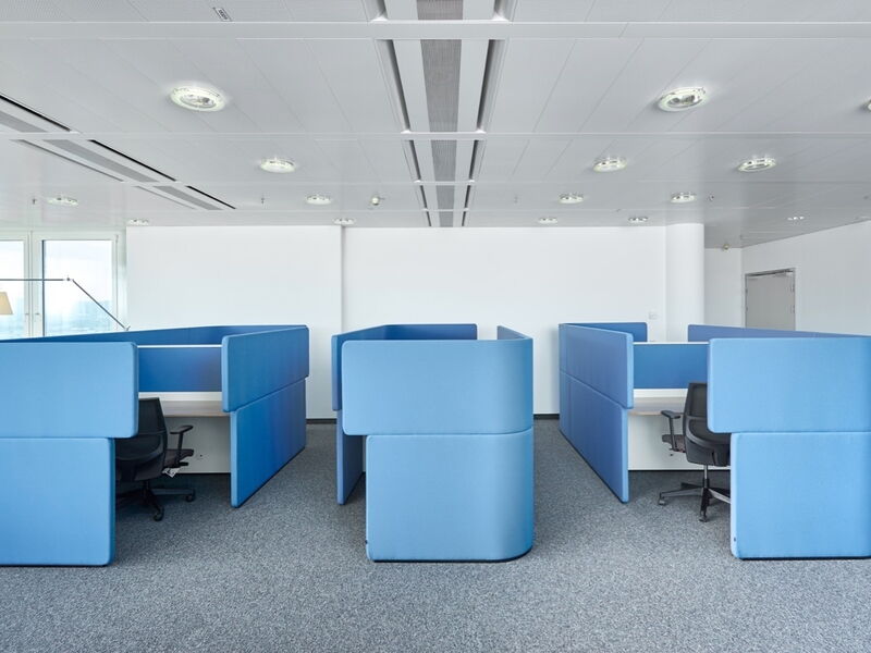 Modern open-plan office interior featuring rows of blue acoustic room dividers, privacy cubicles, and ergonomic office chairs on grey carpet