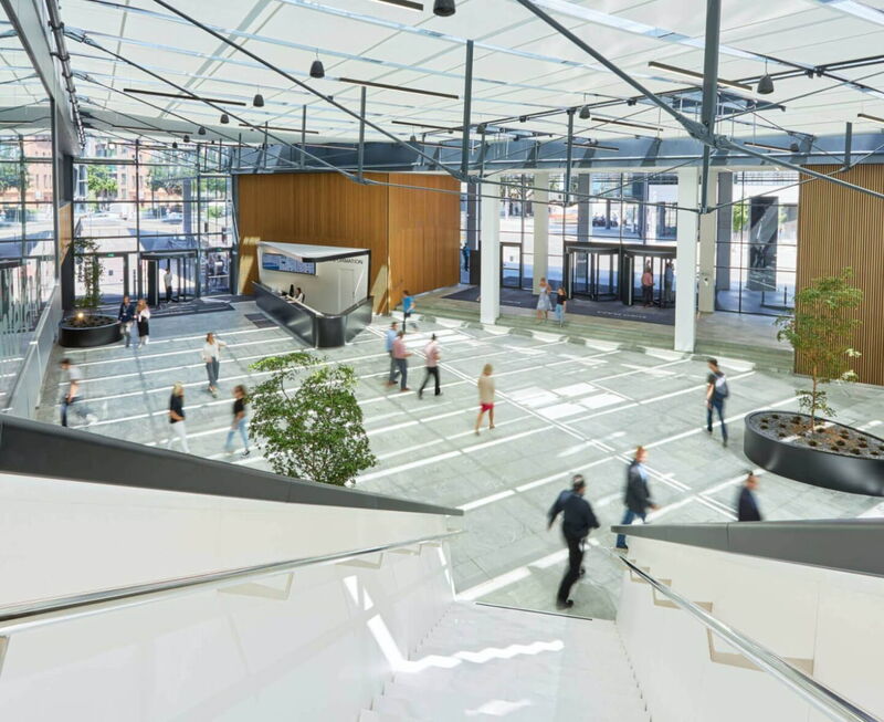 Spacious and bright modern office building lobby with glass facade, reception desk, and people walking, representing professional domizilservice.