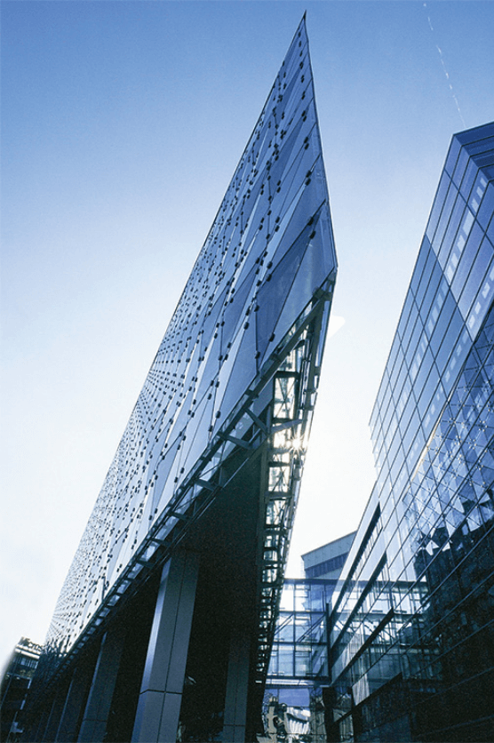 Froschperspektive eines futuristischen Wolkenkratzers aus Glas mit spitzer architektonischer Kante vor klarem blauem Himmel