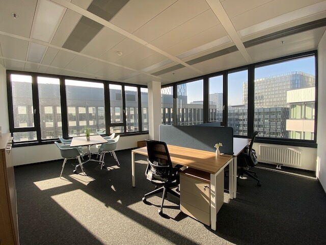 Spacious modern office with large windows, wooden flooring, sleek desks, and comfortable chairs.