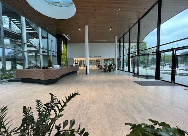 Geräumiges und modernes Bürogebäude Foyer mit eleganter Rezeption, Holzbedeckter Decke, großen Glasfenstern und einer Metalltreppe.