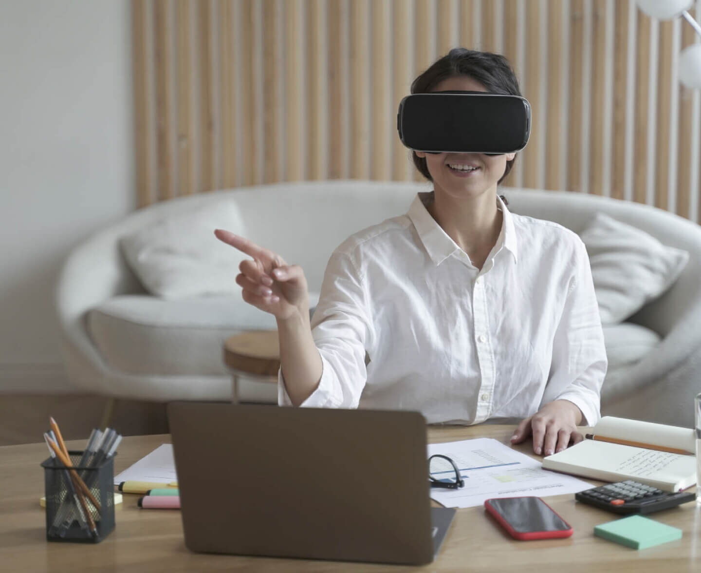 Young businesswoman wearing virtual reality headset while pointing at a screen in a modern office setup with a laptop