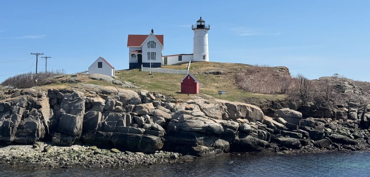 Malerischer Blick auf den Cape Neddick Leuchtturm auf einer felsigen Insel mit Gebäuden unter blauer Himmel, symbolisiert die Freiheit, von überall zu arbeiten.