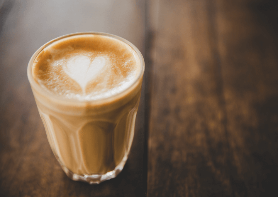 Ein Glas frischer Cappuccino mit feiner Herz-Latte-Art auf einem rustikalen Holztisch