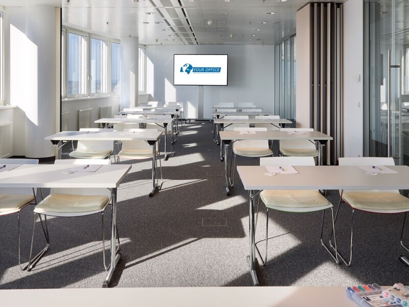 Heller Firmen-Seminarraum mit Reihen von weißen Tischen, bequemen Stühlen und einem Präsentationsbildschirm vorne mit der Aufschrift Your Office.
