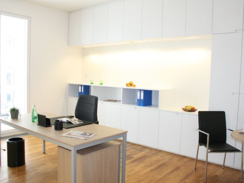 Helles modernes Büro mit Holztisch, schwarzen Stühlen und maßgefertigten weißen Einbauschränken mit indirekter Beleuchtung