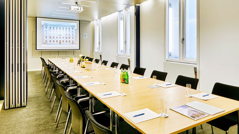 Geräumiger Albert Hall Konferenzraum mit einem langen Holztisch, vorbereitet für eine Präsentation mit Beamerleinwand